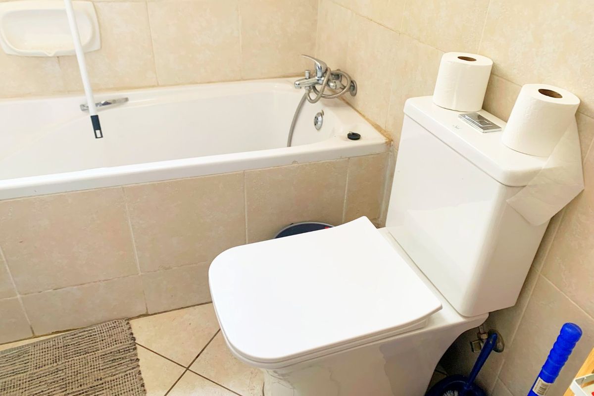 A functional bathroom featuring a built-in bathtub with shower mixer and a dual-flush toilet, finished with neutral ceramic wall and floor tiling.