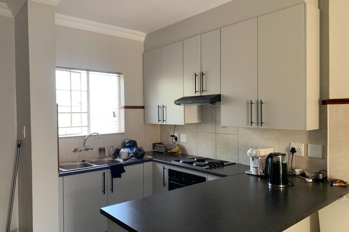 A functional kitchen featuring light-toned cabinetry, dark laminate countertops, a built-in oven with hob, and a tiled splashback with a window view.