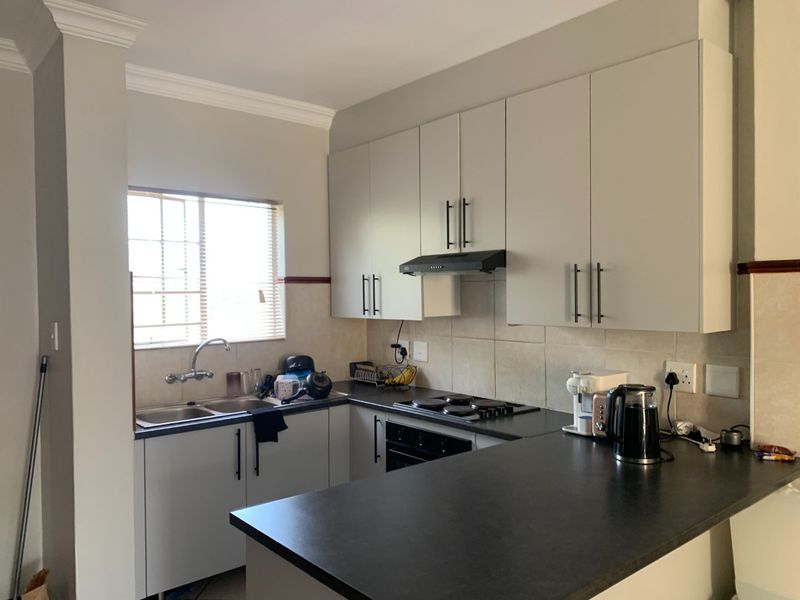 A functional kitchen featuring light-toned cabinetry, dark laminate countertops, a built-in oven with hob, and a tiled splashback with a window view.