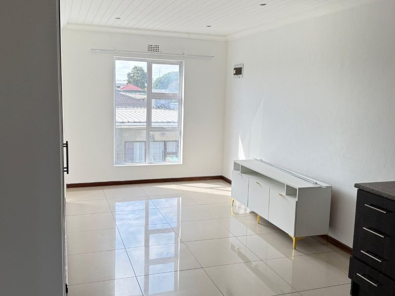 A bright and spacious living area featuring polished tiled flooring, a white tongue and groove ceiling with recessed lighting, and large aluminium-framed windows.