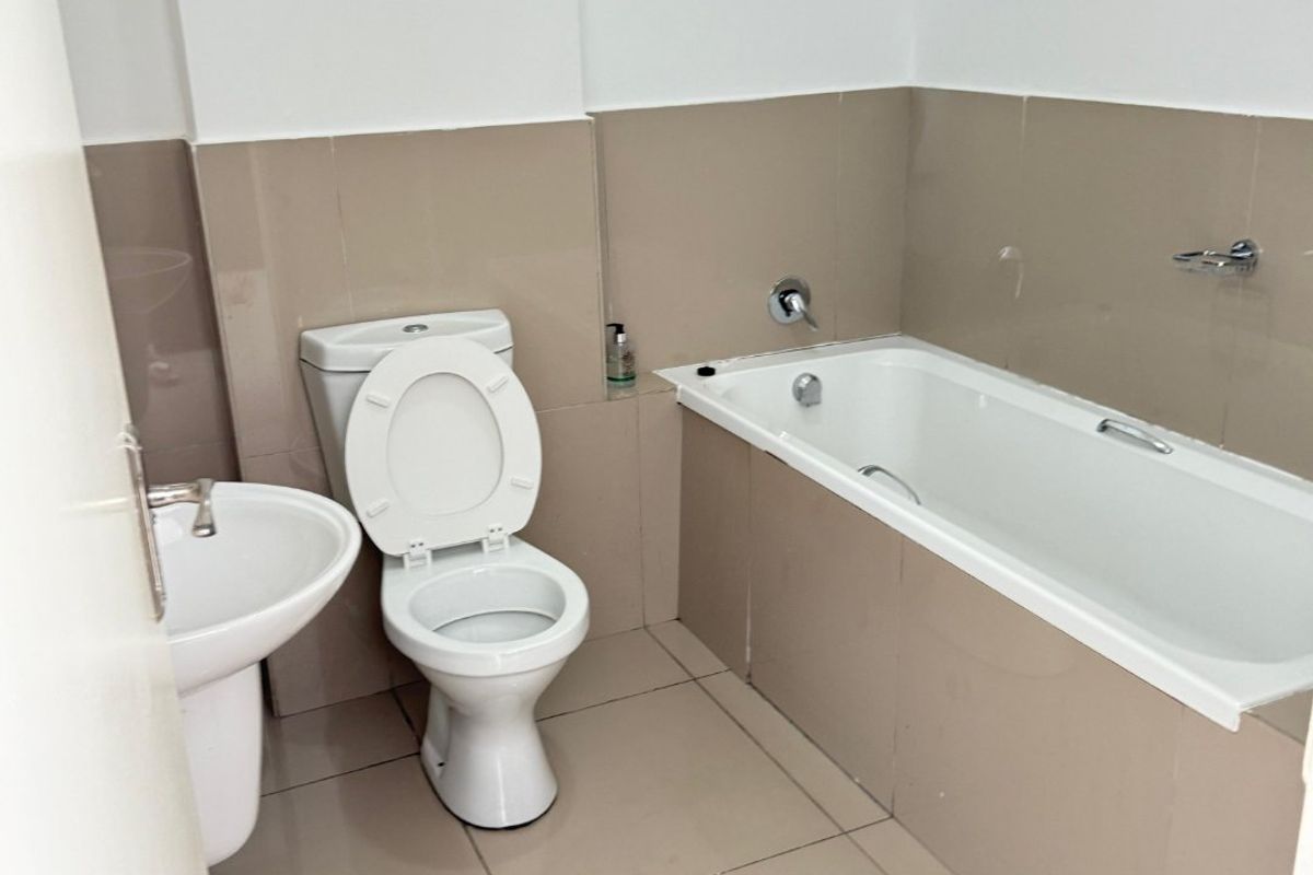 A functional bathroom featuring a pedestal basin, toilet, and a built-in bathtub with neutral wall and floor tiling.