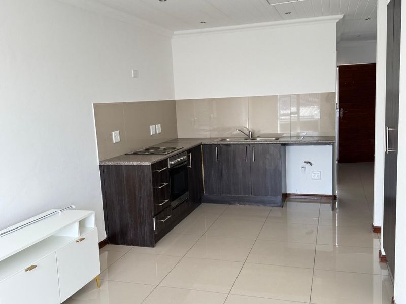 A clean, modern kitchen featuring dark wood cabinetry, granite countertops, built-in oven and hob, and neutral tiled flooring in an open-plan layout.
