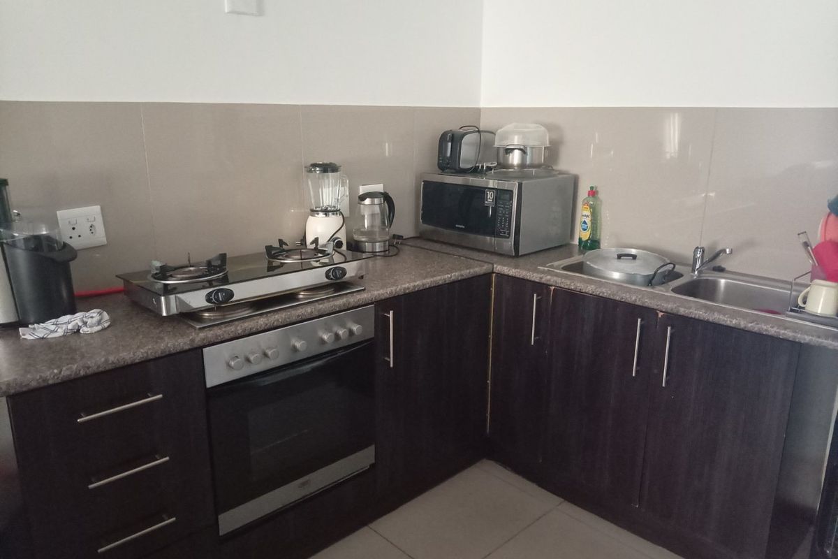 Compact kitchen featuring dark cabinetry, laminate countertops, a built-in oven with gas hob, and a double sink with tiled backsplash.