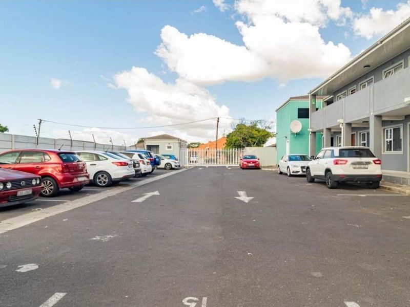 Exterior view of the property featuring a paved parking area, perimeter wall with electric fencing, and secure gated access.