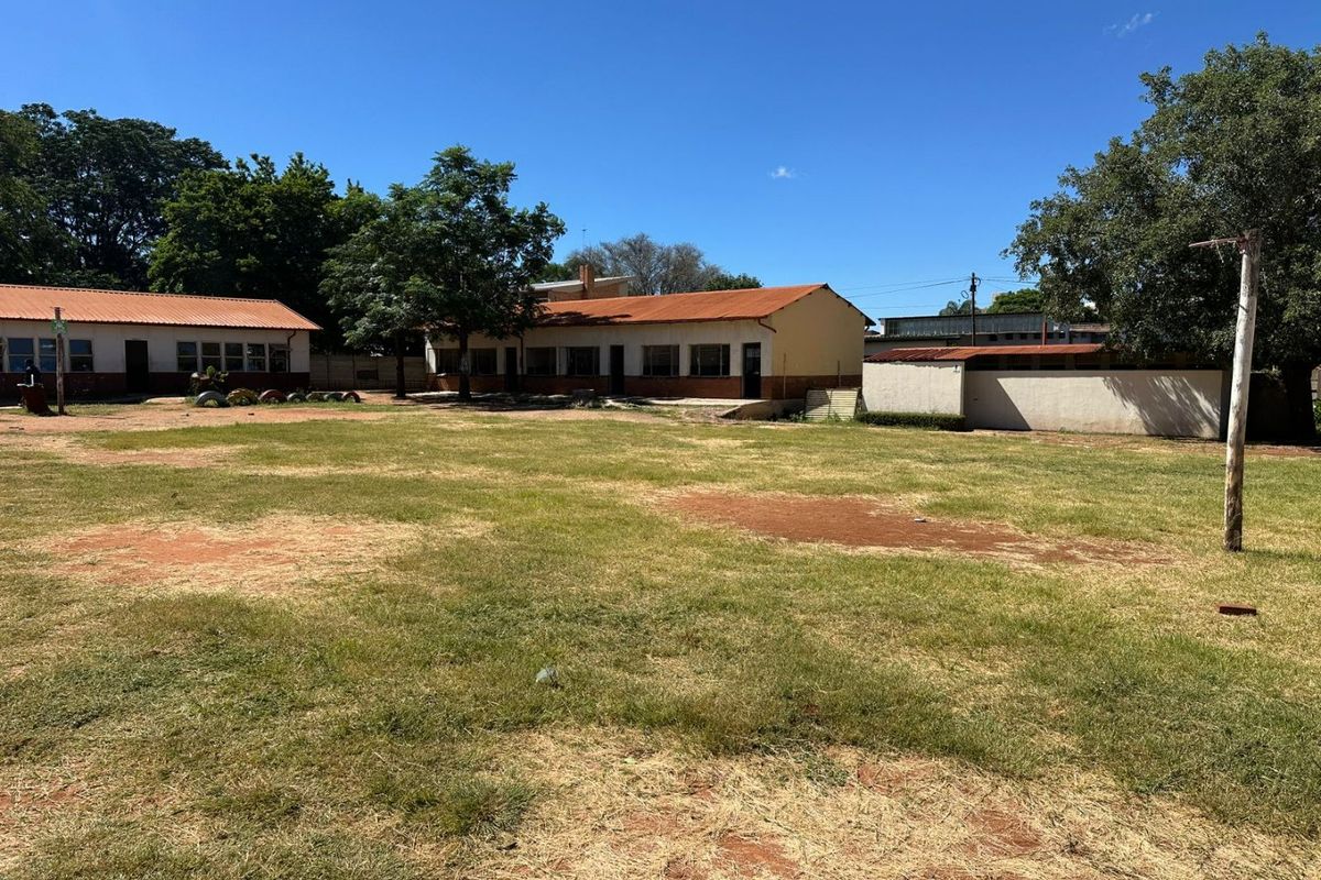 A wide view of a commercial property grounds featuring multiple single-story buildings with corrugated metal roofs and a large open grass field.
