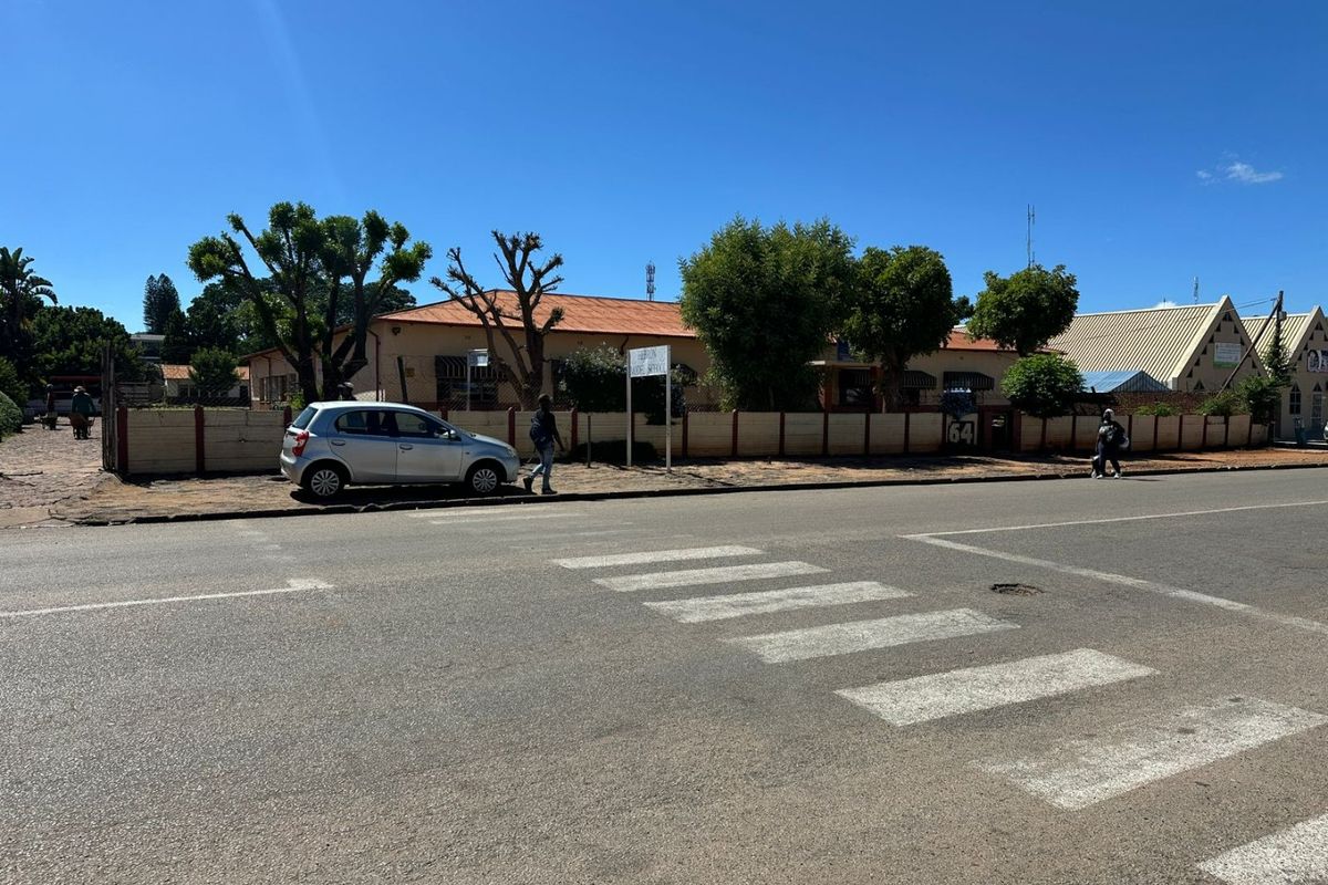 Street view of the commercial property frontage featuring a perimeter wall, gated entrance, and direct access from the main road with a pedestrian crossing.