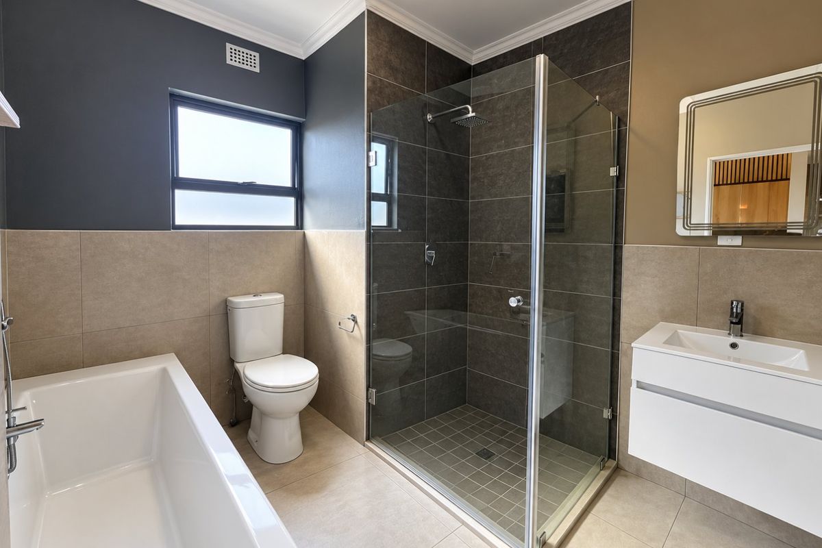 Modern bathroom featuring a glass-enclosed shower, a built-in bathtub, a wall-mounted vanity with basin, and neutral-toned tiled finishes.