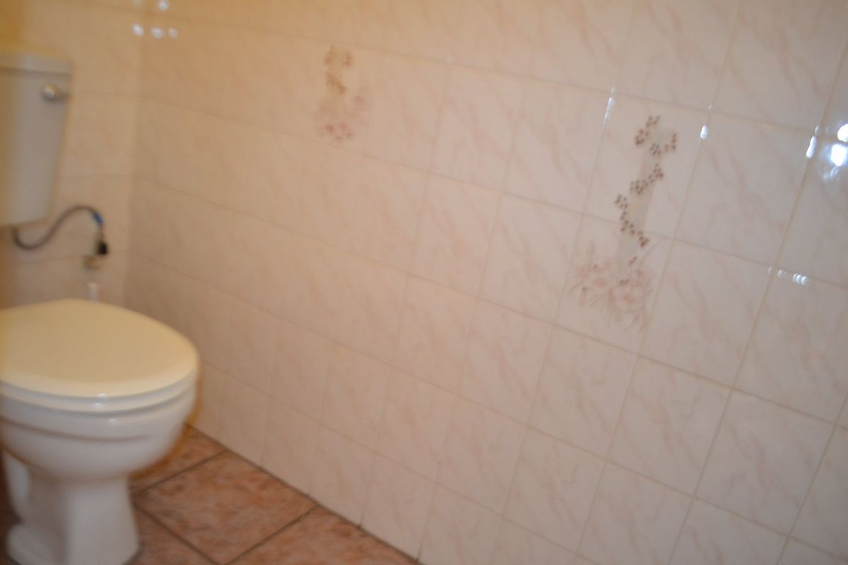 A small bathroom featuring a standard toilet with dated ceramic wall and floor tiling.