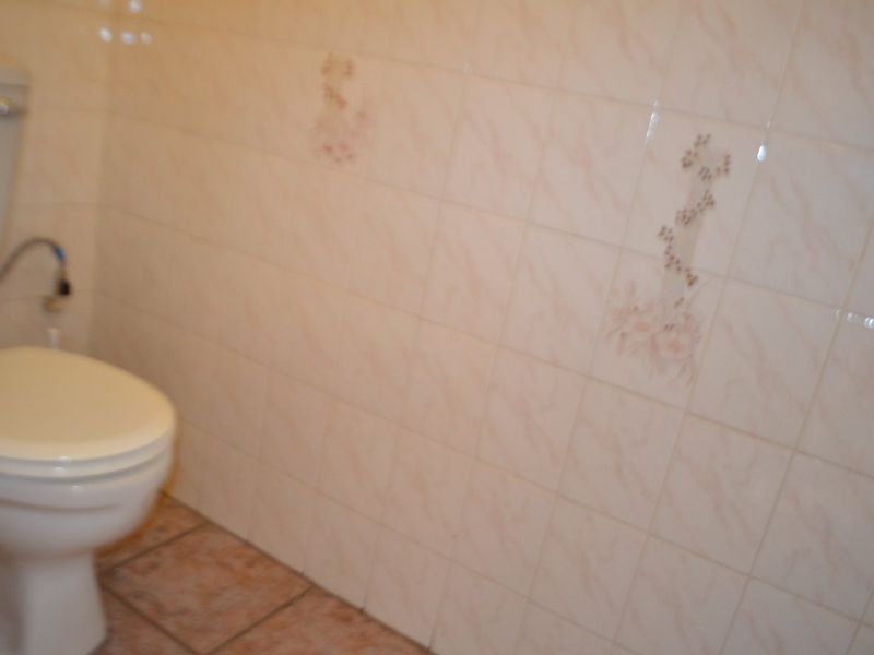 A small bathroom featuring a standard toilet with dated ceramic wall and floor tiling.