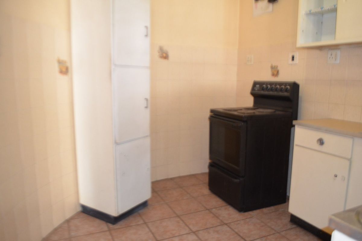 A functional kitchen area featuring tiled flooring, a built-in pantry cupboard, and a freestanding stove with wall-mounted cabinetry.