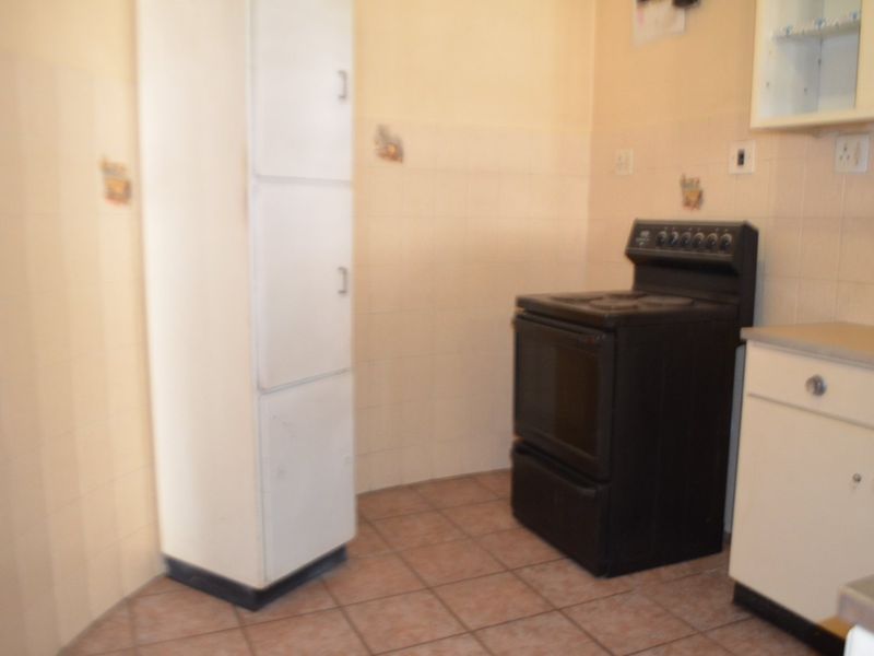 A functional kitchen area featuring tiled flooring, a built-in pantry cupboard, and a freestanding stove with wall-mounted cabinetry.