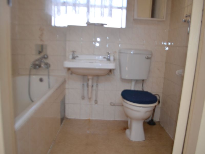 A dated bathroom featuring a standard bathtub, wall-mounted basin, and toilet with tiled walls, requiring modernization and cosmetic updates.
