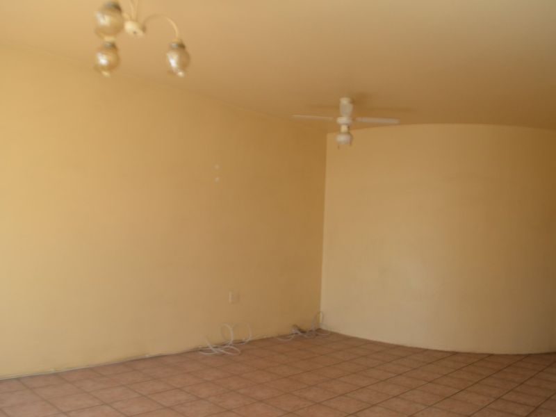 An empty living room featuring tiled flooring, a ceiling fan, and a distinctive curved wall design, ready for personalization.