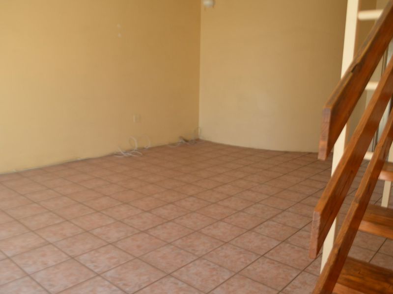 An empty living room featuring tiled flooring and a wooden staircase, requiring minor cosmetic updates to the walls.