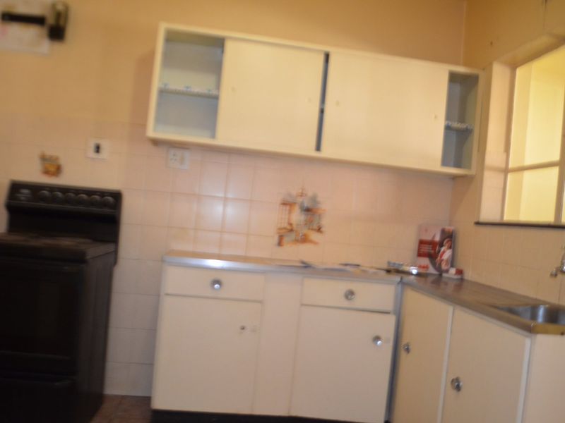 A dated kitchen featuring original built-in cabinetry, a stainless steel sink, and tiled backsplash, offering potential for a modern renovation.