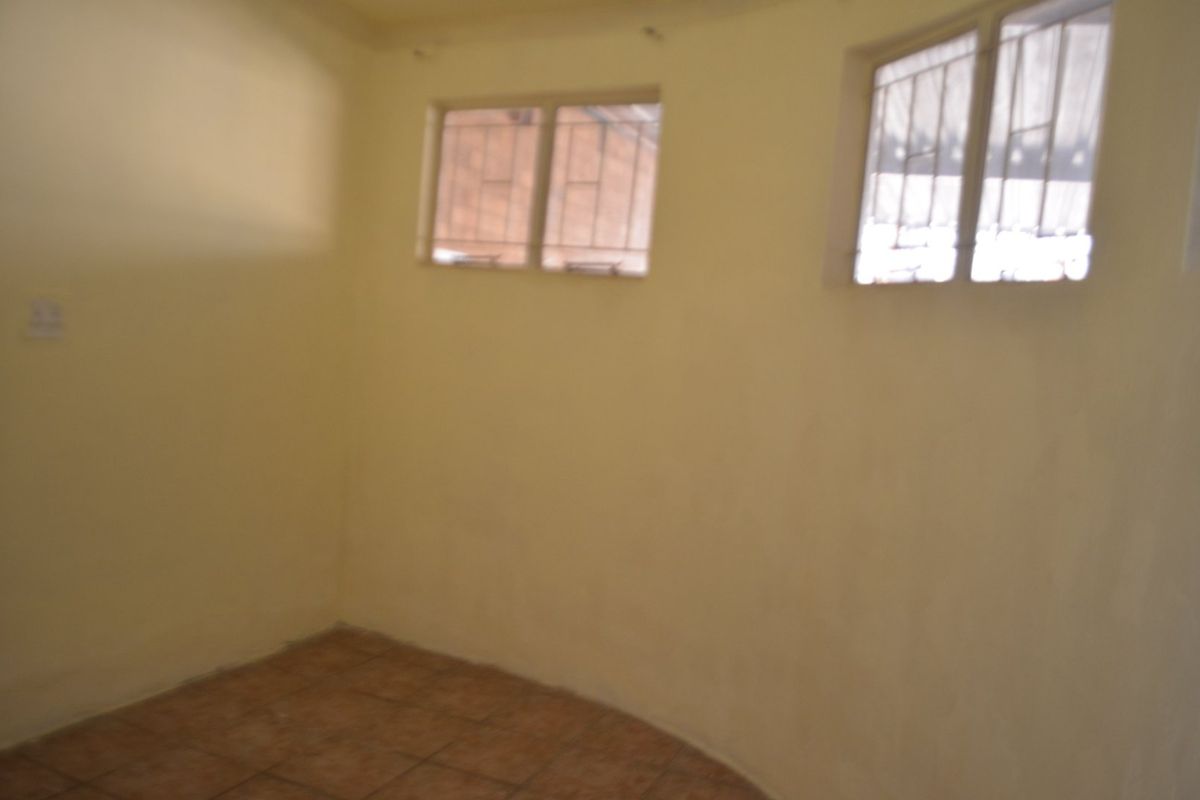 An empty bedroom featuring tiled flooring and windows fitted with security bars, offering a blank canvas for potential renovation.