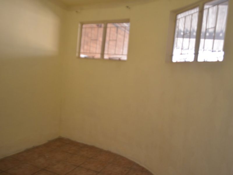 An empty bedroom featuring tiled flooring and windows fitted with security bars, offering a blank canvas for potential renovation.