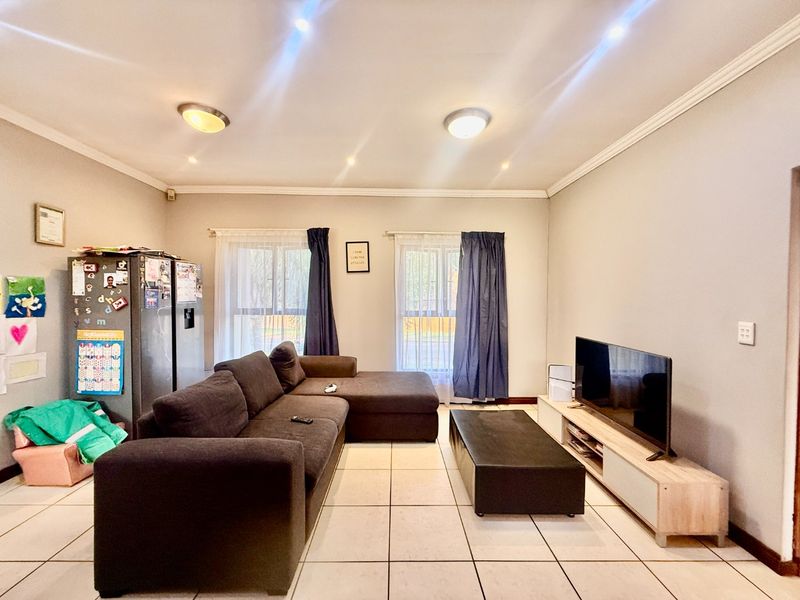 An open-plan living area featuring neutral tiled flooring, recessed downlighting, and large windows that provide natural light to the space.