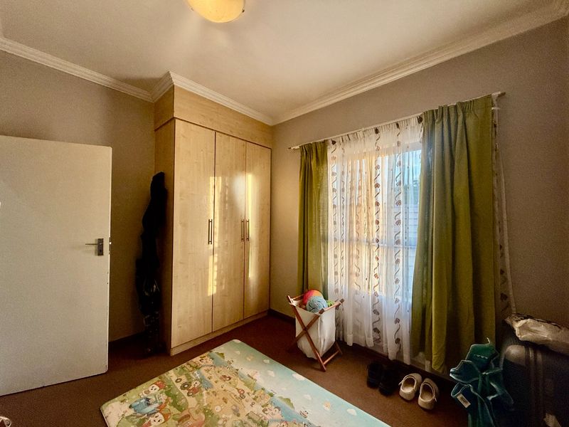 A bedroom featuring built-in wooden wardrobes, carpeted flooring, and decorative ceiling cornicing, providing a functional space with natural light.