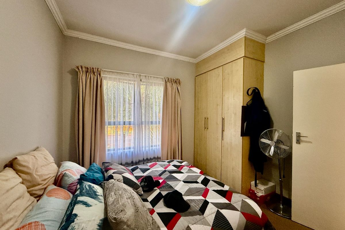 A functional bedroom featuring built-in wooden cupboards, decorative ceiling cornicing, and a window with curtain tracks.