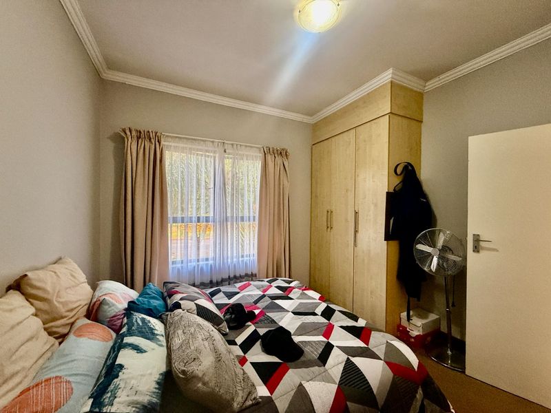 A functional bedroom featuring built-in wooden cupboards, decorative ceiling cornicing, and a window with curtain tracks.