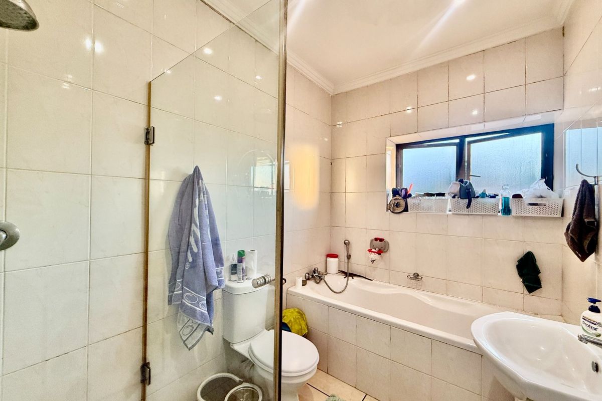 A functional bathroom featuring a combined shower and bathtub, pedestal washbasin, and toilet with full-height wall tiling.