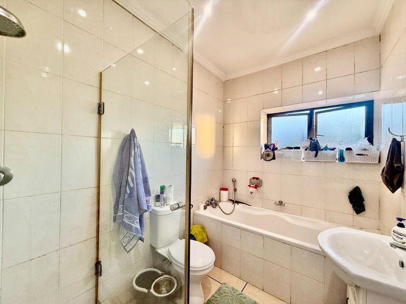 A functional bathroom featuring a combined shower and bathtub, pedestal washbasin, and toilet with full-height wall tiling.