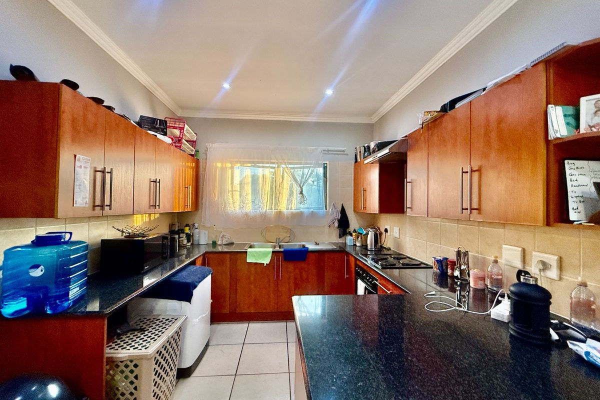 A functional kitchen featuring granite countertops, ample wooden cabinetry, a built-in gas hob with extractor fan, and tiled flooring.