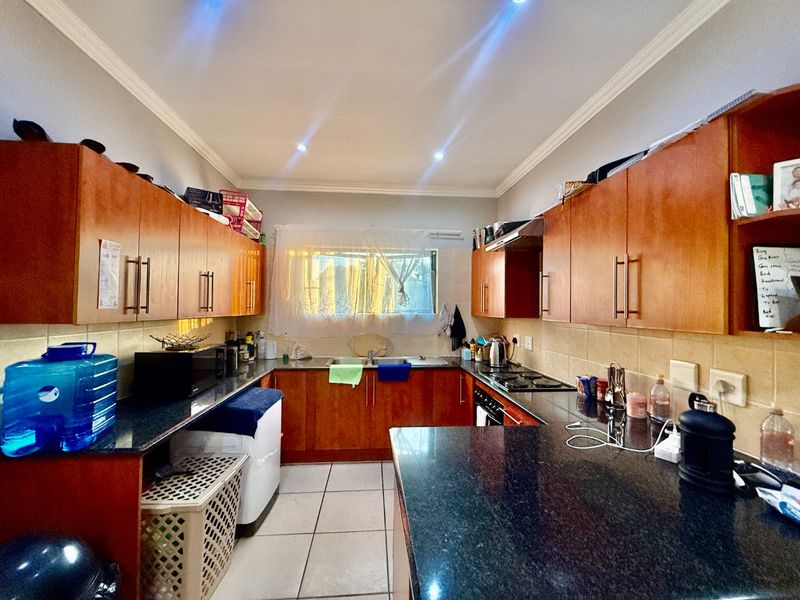 A functional kitchen featuring granite countertops, ample wooden cabinetry, a built-in gas hob with extractor fan, and tiled flooring.