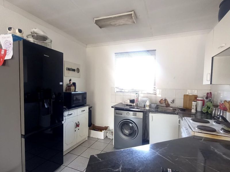 A functional kitchen featuring tiled flooring, built-in cabinetry, a stainless steel sink, and an electric hob with integrated laundry appliance space.