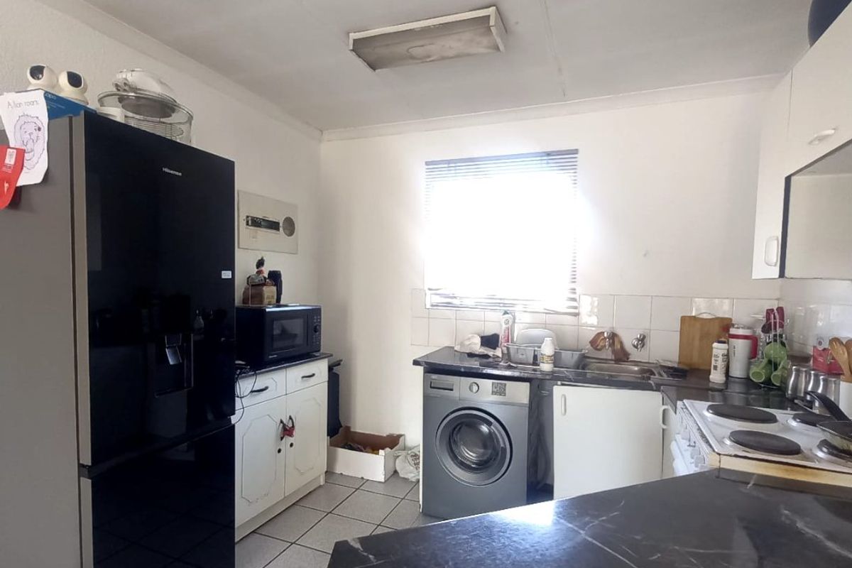 A functional kitchen featuring tiled flooring, built-in cabinetry, a stainless steel sink, and an electric hob with integrated laundry appliance space.