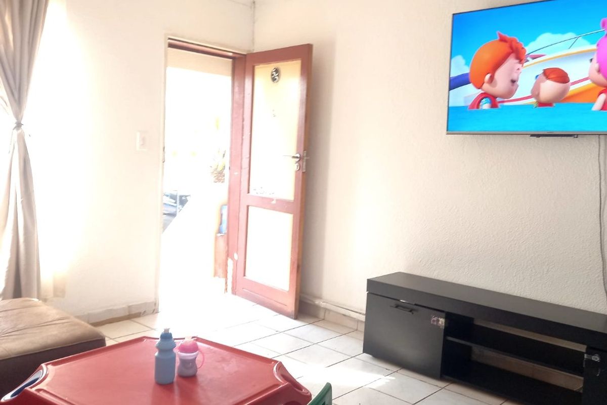 A living room area featuring tiled flooring and a wall-mounted television, providing a functional space with direct access to the exterior.