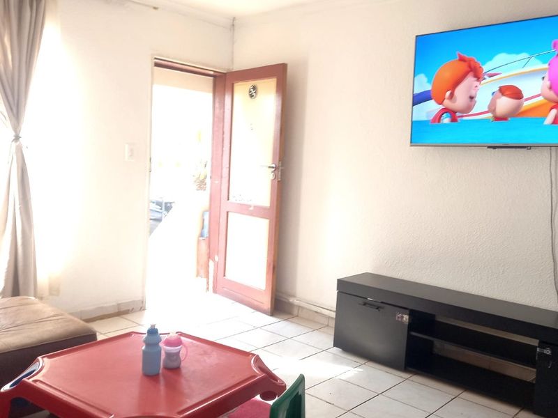 A living room area featuring tiled flooring and a wall-mounted television, providing a functional space with direct access to the exterior.