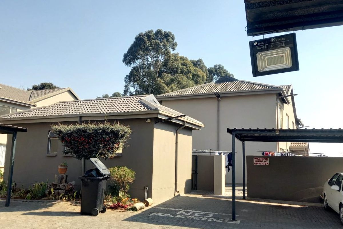 Exterior view of the apartment complex featuring a paved driveway, covered carport parking, and well-maintained building facades with tiled roofing.