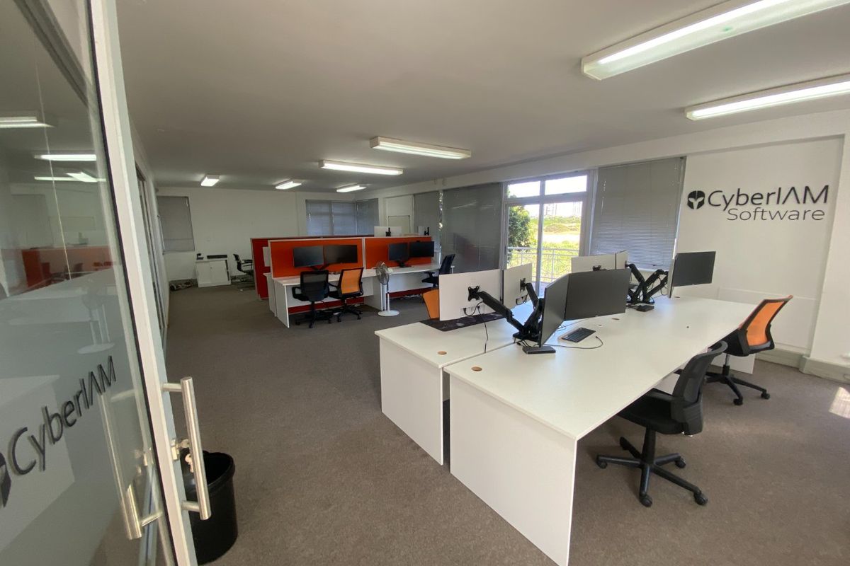 A professional open-plan office space featuring carpeted flooring, fluorescent lighting, and large windows with venetian blinds, suitable for a collaborative work environment.