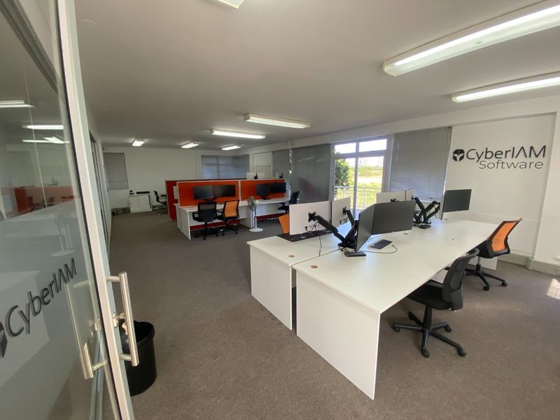 A professional open-plan office space featuring carpeted flooring, fluorescent lighting, and large windows with venetian blinds, suitable for a collaborative work environment.