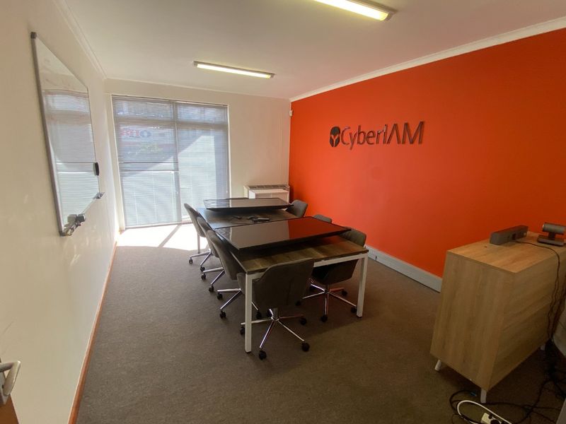 A functional office space featuring carpeted flooring, fluorescent lighting, a wall-mounted whiteboard, and an air conditioning unit, suitable for professional use.