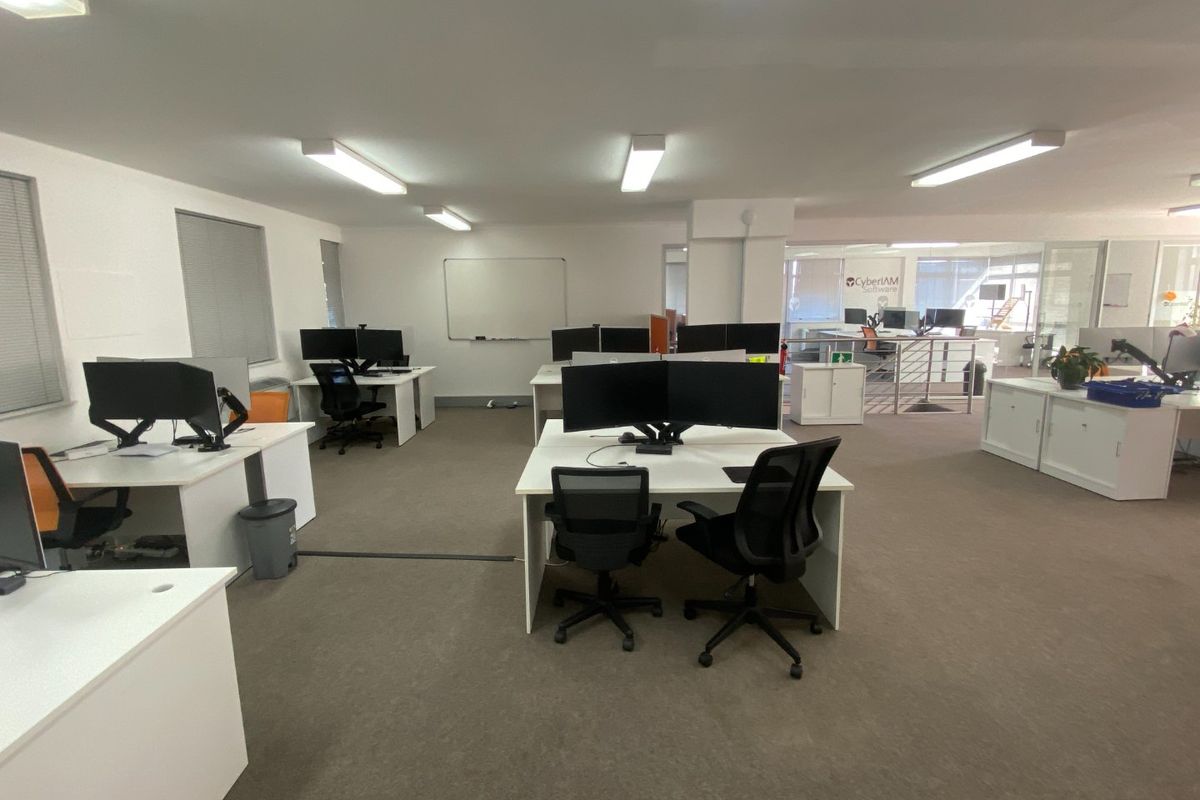 Open-plan commercial office space featuring carpeted flooring, fluorescent lighting, and glass partitions, providing a functional and professional work environment.