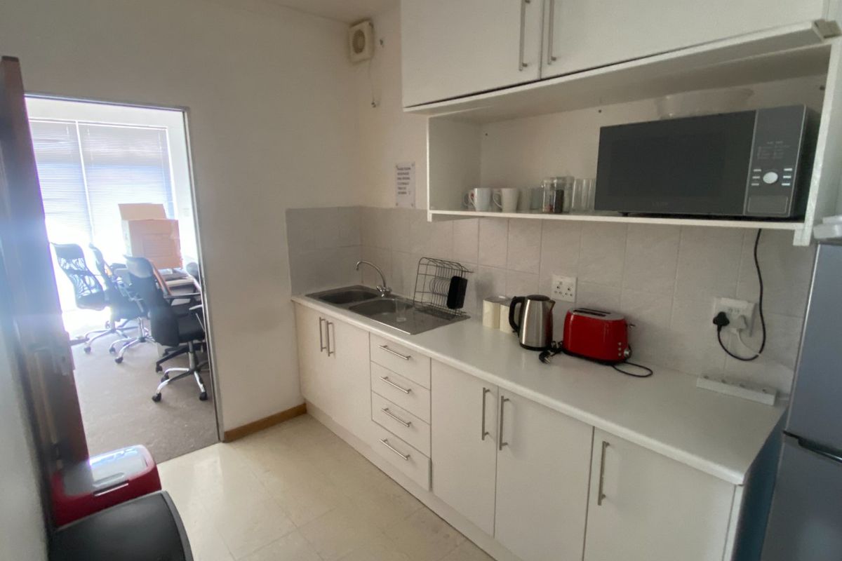 A functional kitchenette featuring white built-in cabinetry, a stainless steel sink, tiled backsplash, and dedicated space for a microwave.