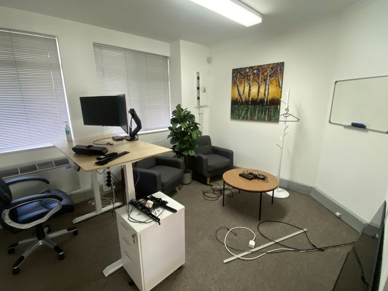 A functional commercial office space featuring neutral carpeting, venetian blinds, and overhead fluorescent lighting, suitable for a professional work environment.