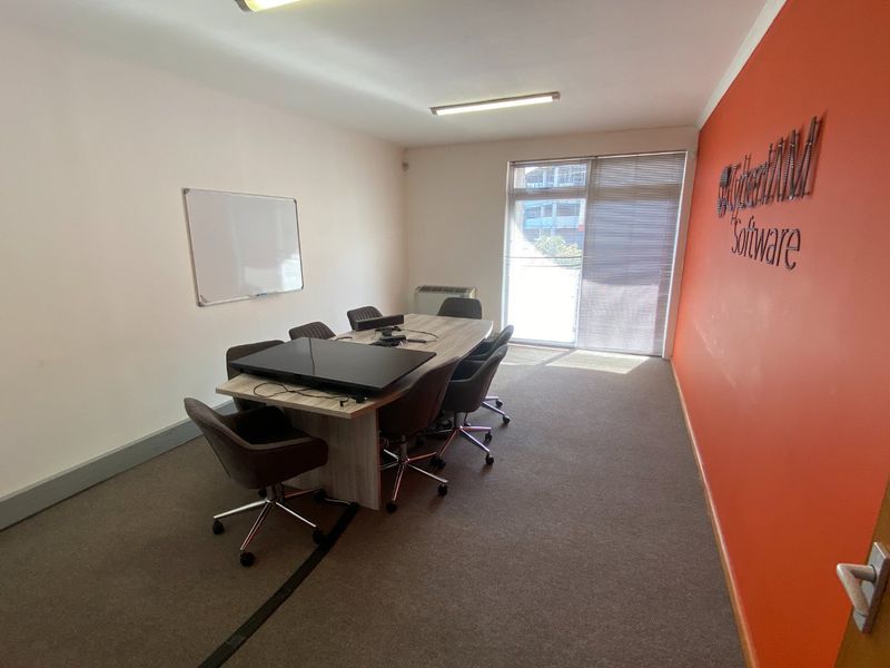 A functional office space featuring carpeted flooring, a wall-mounted air conditioning unit, and an accent wall, suitable for a professional meeting or workspace.