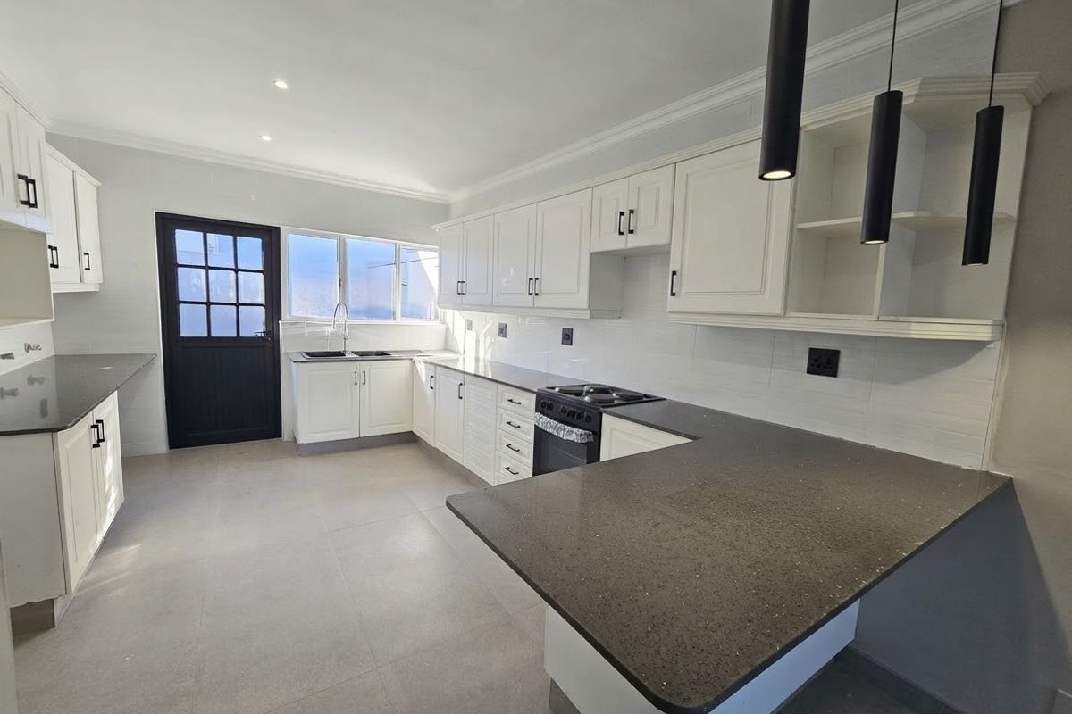 A bright, modern kitchen featuring white cabinetry, dark stone countertops, integrated appliances, and tiled flooring, offering a clean and functional workspace.