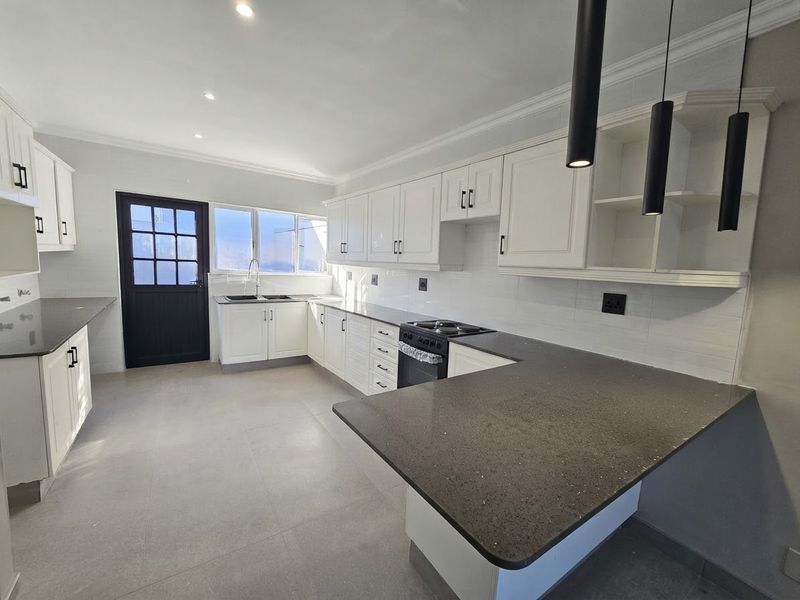 A bright, modern kitchen featuring white cabinetry, dark stone countertops, integrated appliances, and tiled flooring, offering a clean and functional workspace.
