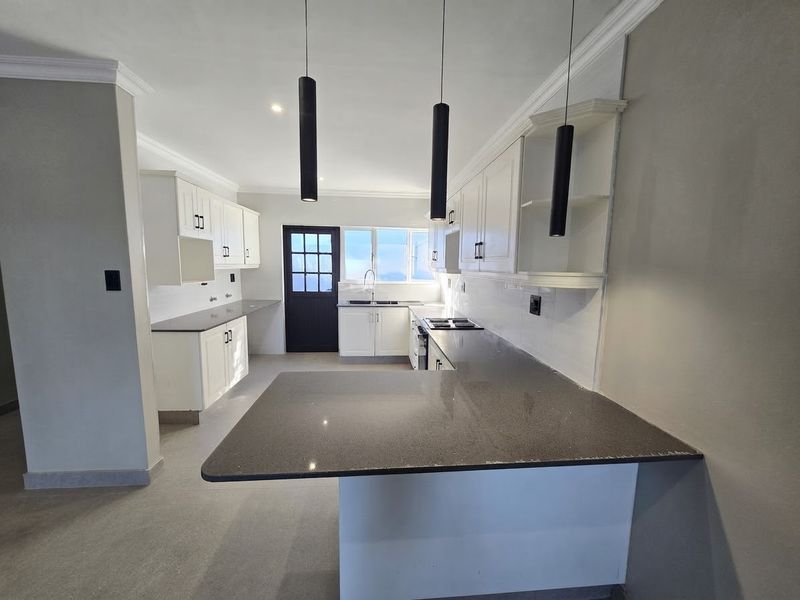 A modern, clean kitchen featuring white cabinetry, dark stone countertops, a tiled backsplash, and contemporary pendant lighting, offering a functional and bright workspace.