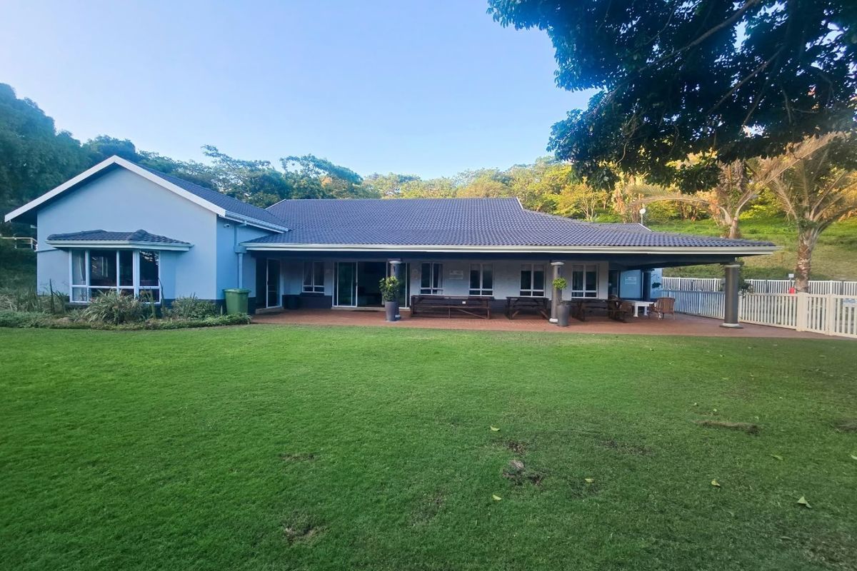 Spacious rear exterior view featuring a large manicured lawn, a covered patio area with tiled flooring, and a well-maintained single-story house structure.