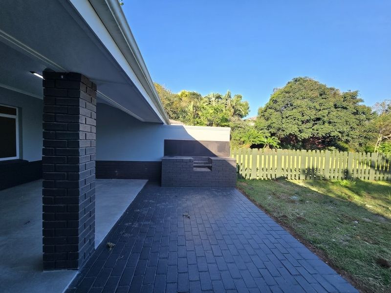 A clean, covered patio area featuring a built-in brick braai, paved flooring, and direct access to the garden.