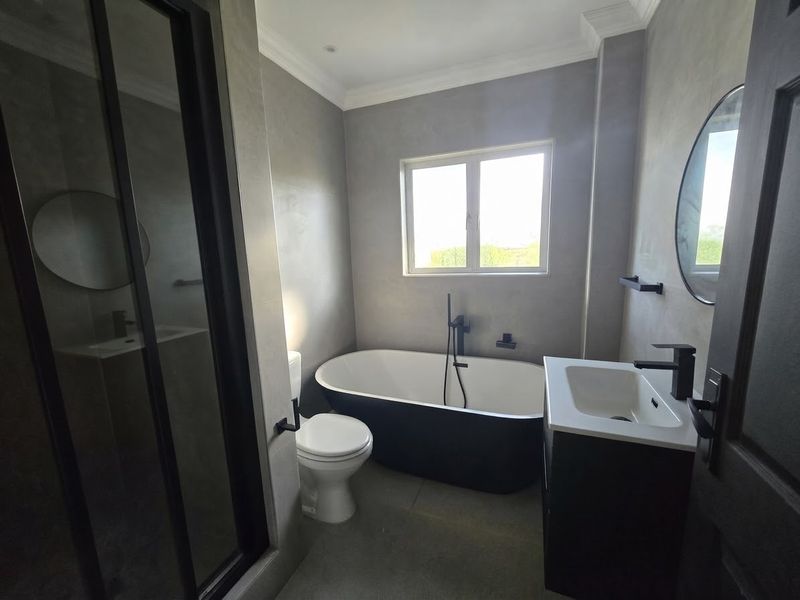 Modern bathroom featuring a sleek freestanding bathtub, glass-enclosed shower, vanity basin, and contemporary black matte fixtures with a polished cement-style wall finish.