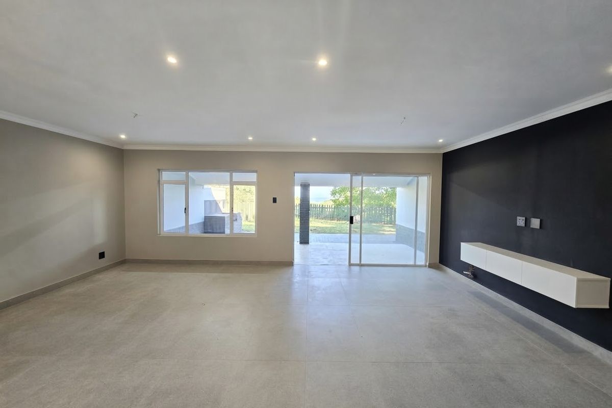 Spacious, modern living area featuring neutral tiled floors, a sleek floating media console, and large sliding doors providing seamless access to the outdoor patio.