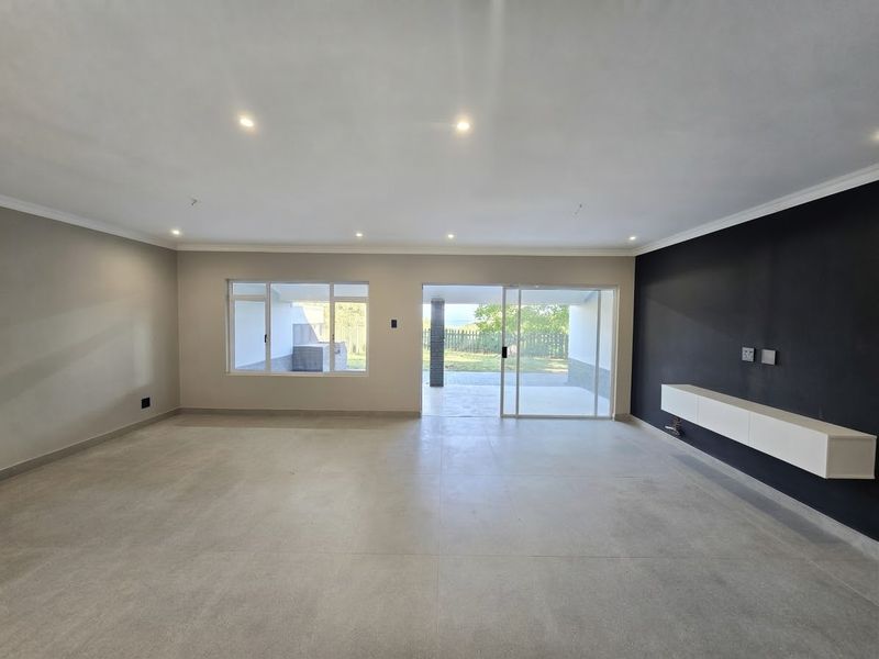 Spacious, modern living area featuring neutral tiled floors, a sleek floating media console, and large sliding doors providing seamless access to the outdoor patio.