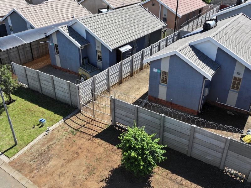 Aerial view of residential properties featuring tiled roofs, solar geysers, and secure precast concrete boundary walls with razor wire fencing.